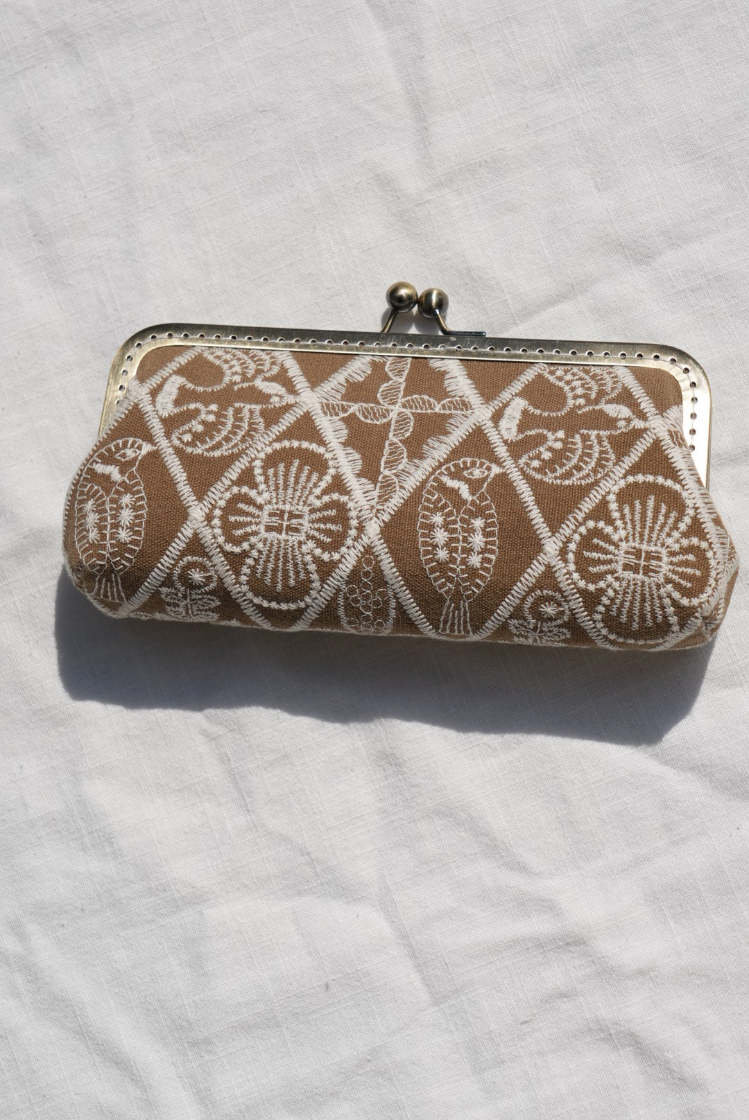 A vintage-style clutch purse with a brown and white lace pattern, resting on a white fabric background.